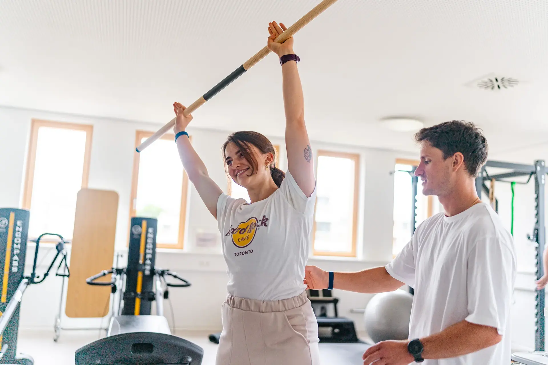 Physiotherapeut unterstützt eine Patientin bei Dehnübungen mit einer Stange zur Verbesserung der Flexibilität und Mobilität.