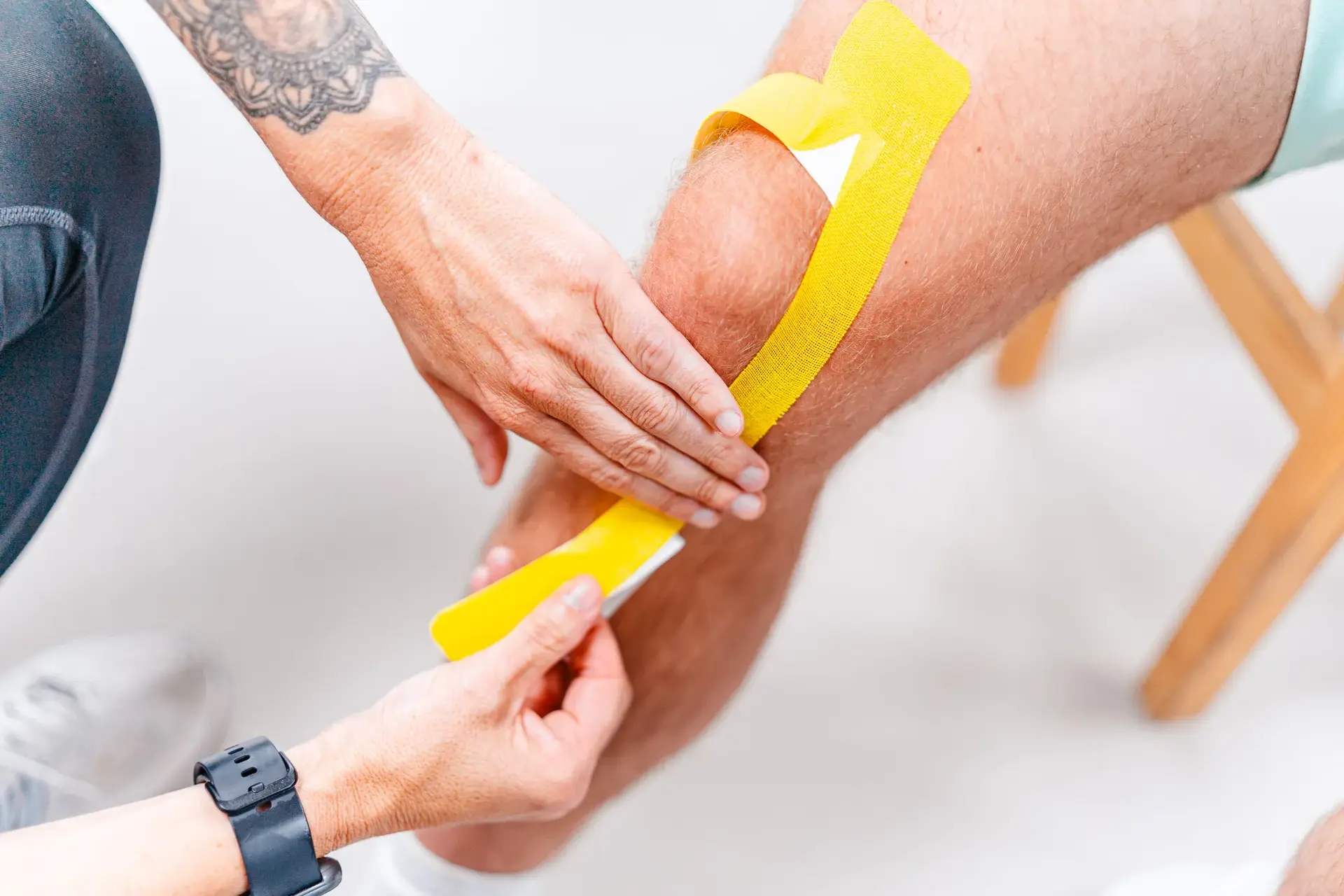 Therapeutin bringt Kinesio-Tape an das Knie eines Patienten an, um die Muskulatur zu stabilisieren und die Rehabilitation zu unterstützen.