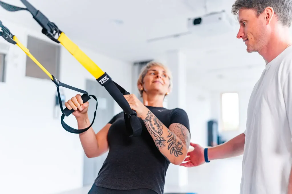 Eine Person führt ein TRX-Training unter Anleitung eines Trainers durch.